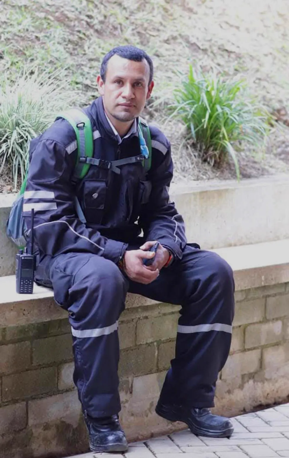 Un hombre con camisa azul de uniforme de seguridad, de pie en una habitación con cuadros de colores en la pared.