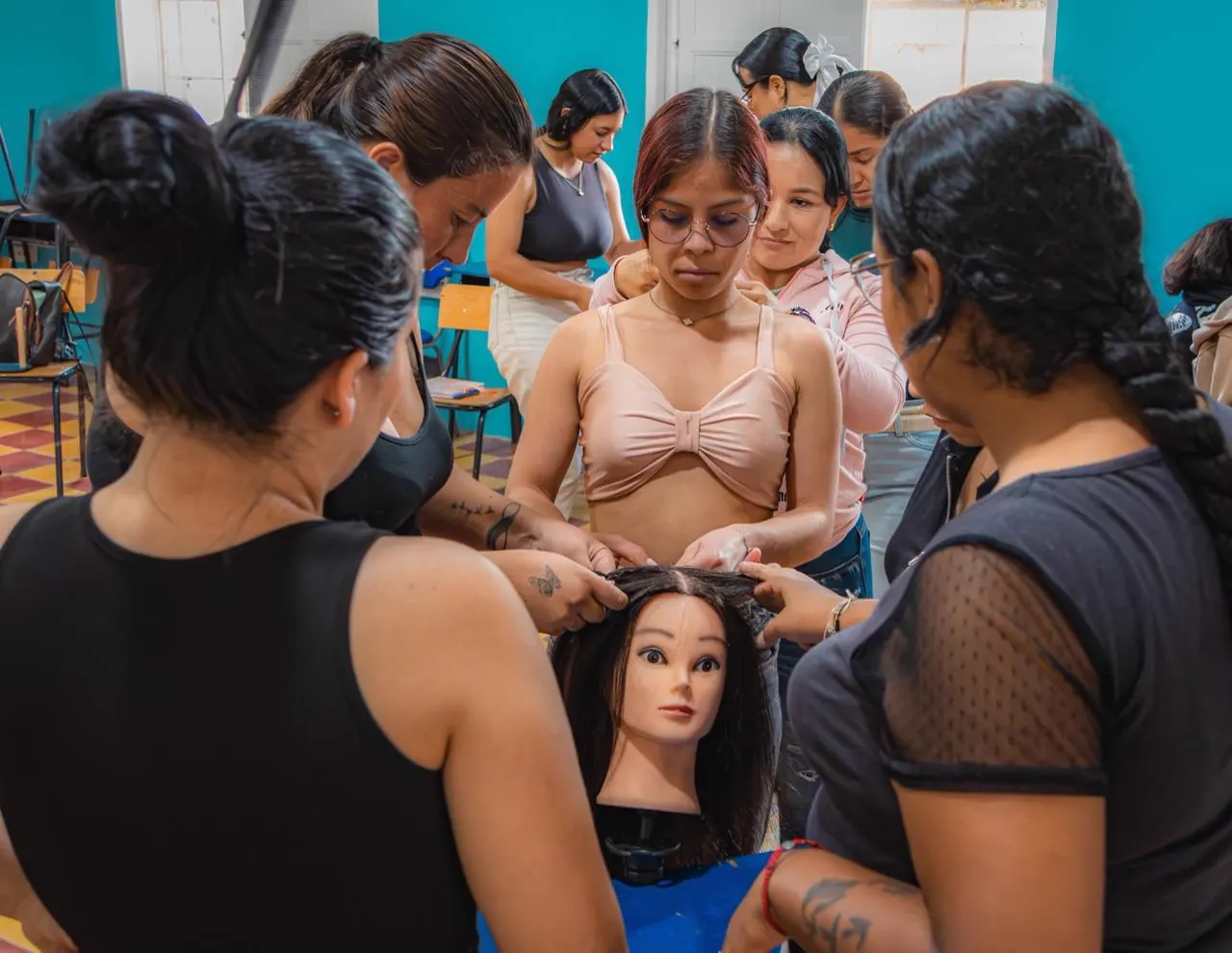 Grupo de mujeres practica peinados sobre una cabeza de maniquí en un salón de clases.