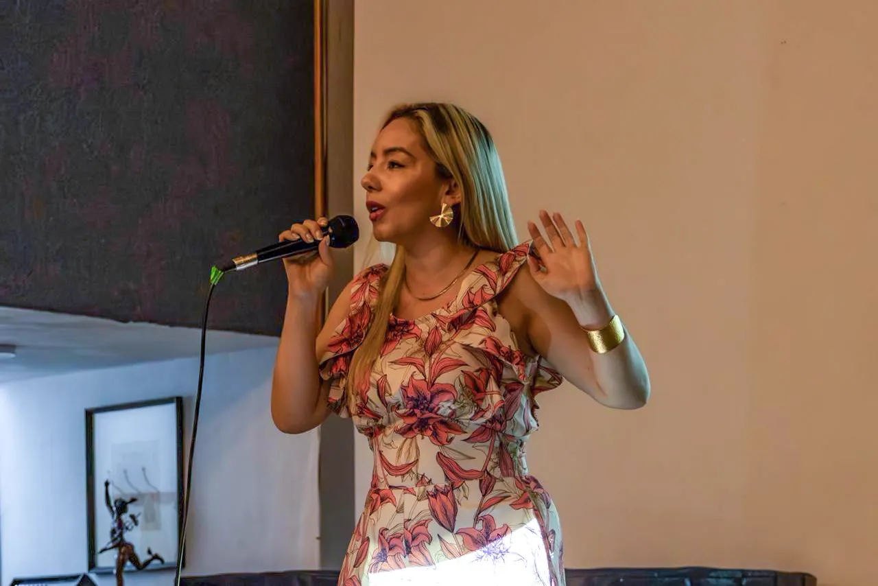 Elisa Krack habla con un micrófono en la mano y gesticula con la otra, vestida con una blusa de flores.