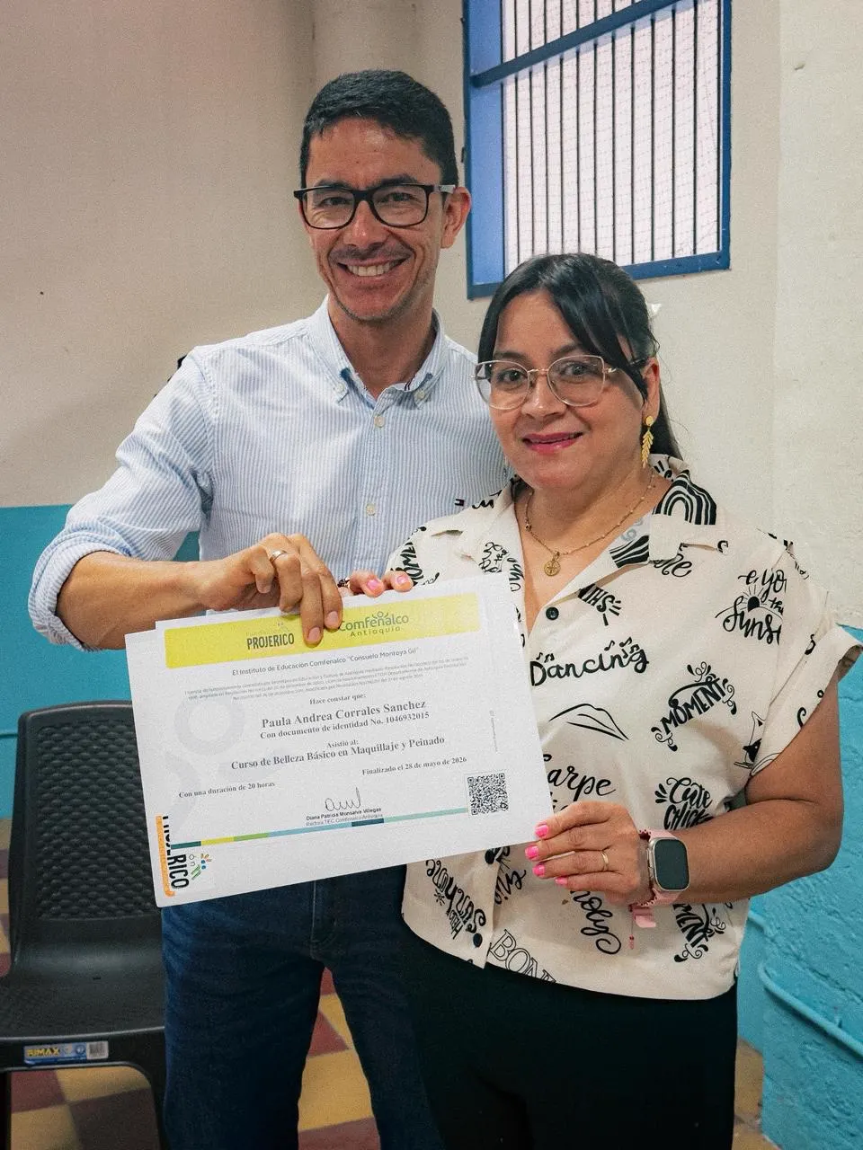 Un hombre con gafas y camisa clara y una mujer con gafas y blusa estampada sostienen juntos un certificado.
