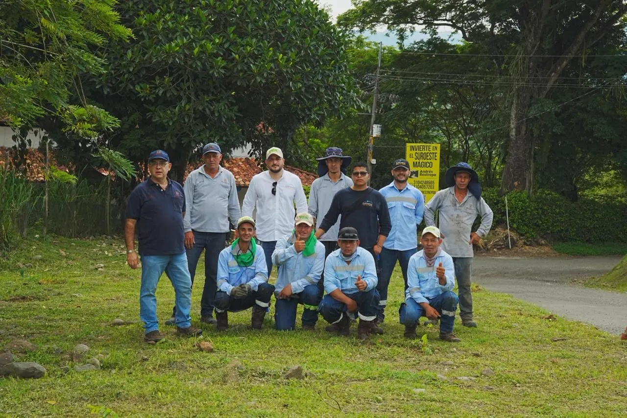 Grupo de once hombres, varios con camisas de dotación y gorras, posa en una zona verde junto a una vía, cinco de ellos agachados al frente.