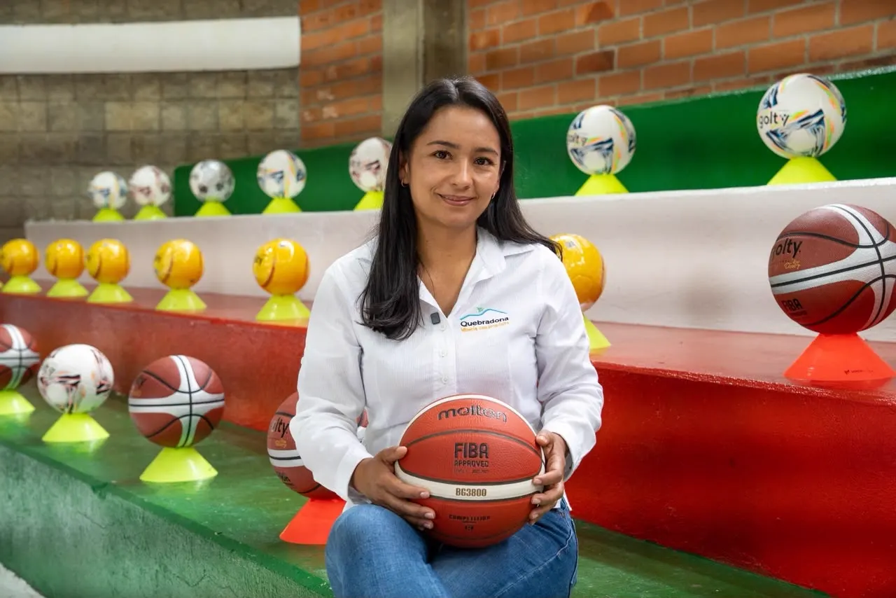 Ángela Montoya, de camisa blanca, sentada en unas graderías sostiene un balón de baloncesto, rodeada de balones sobre conos.