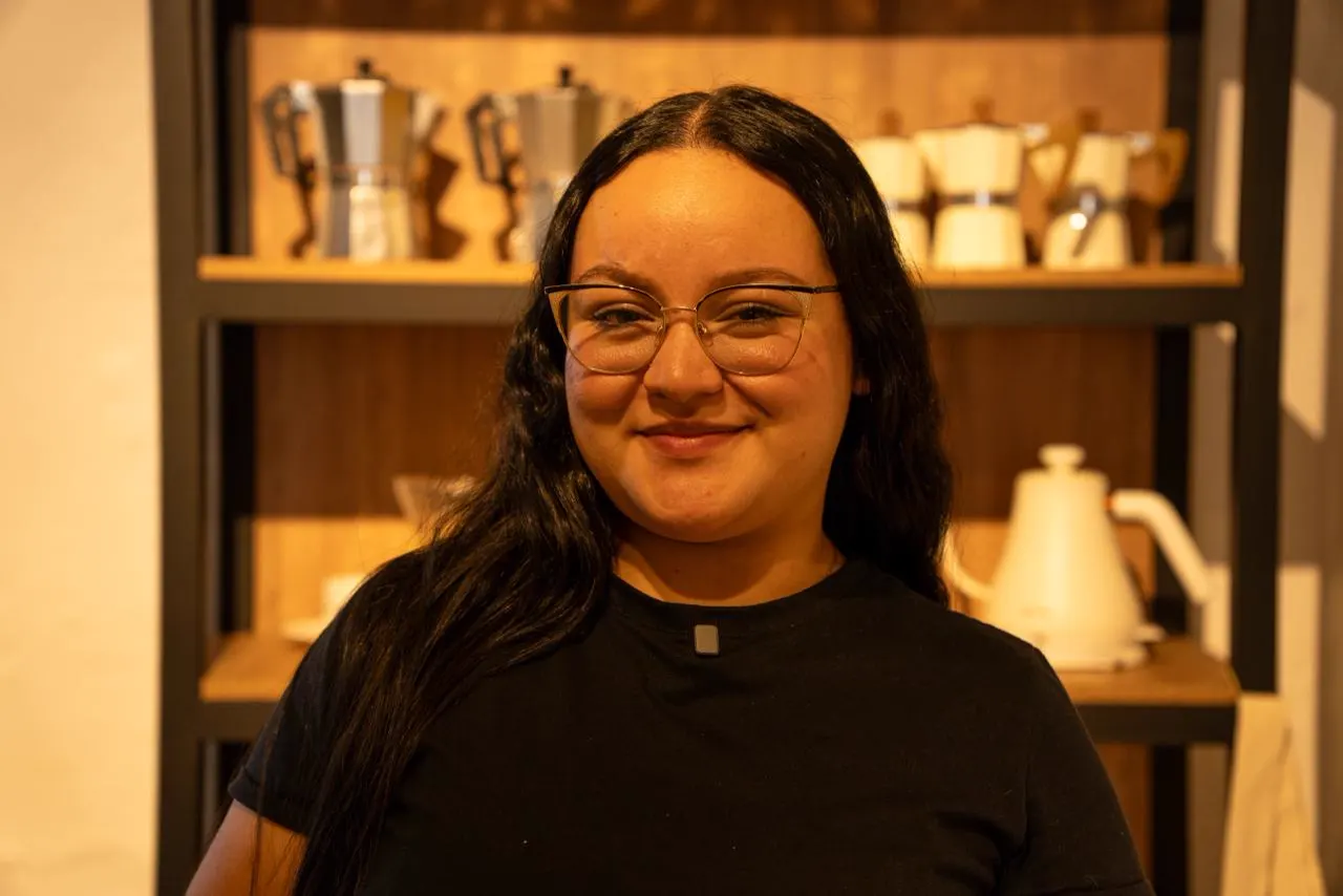 Retrato de una participante del curso de Arte Latte junto a una estantería con cafeteras.