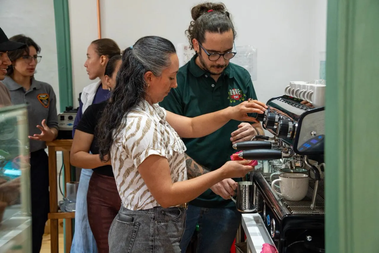 Participantes del curso de Arte Latte preparan café en una máquina de espresso durante la clase de cierre.